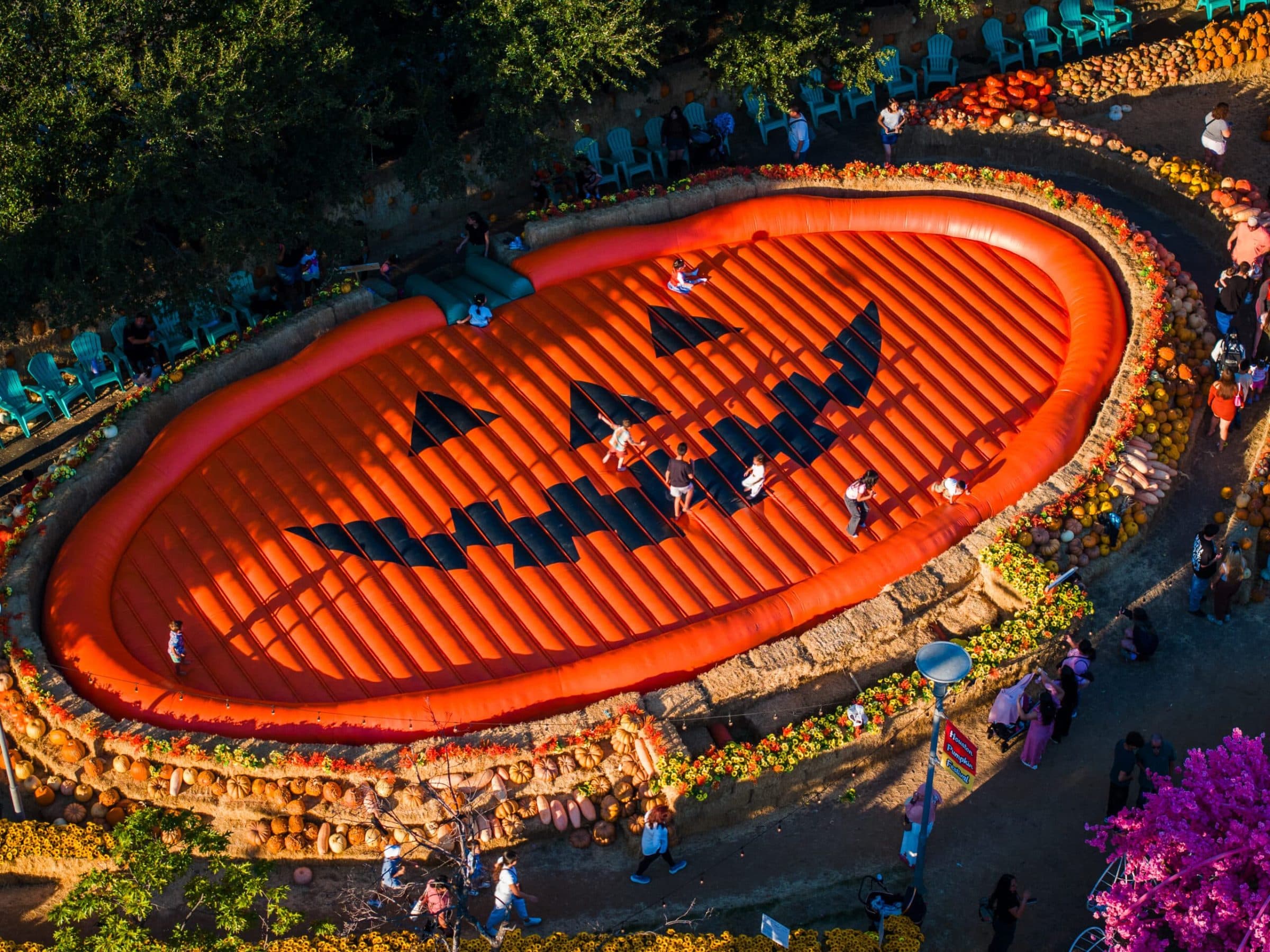 The giant inflatable jack-o'-lantern bounce pillow glowing at sunset, ringed by hay bales, pumpkins and turquoise chairs